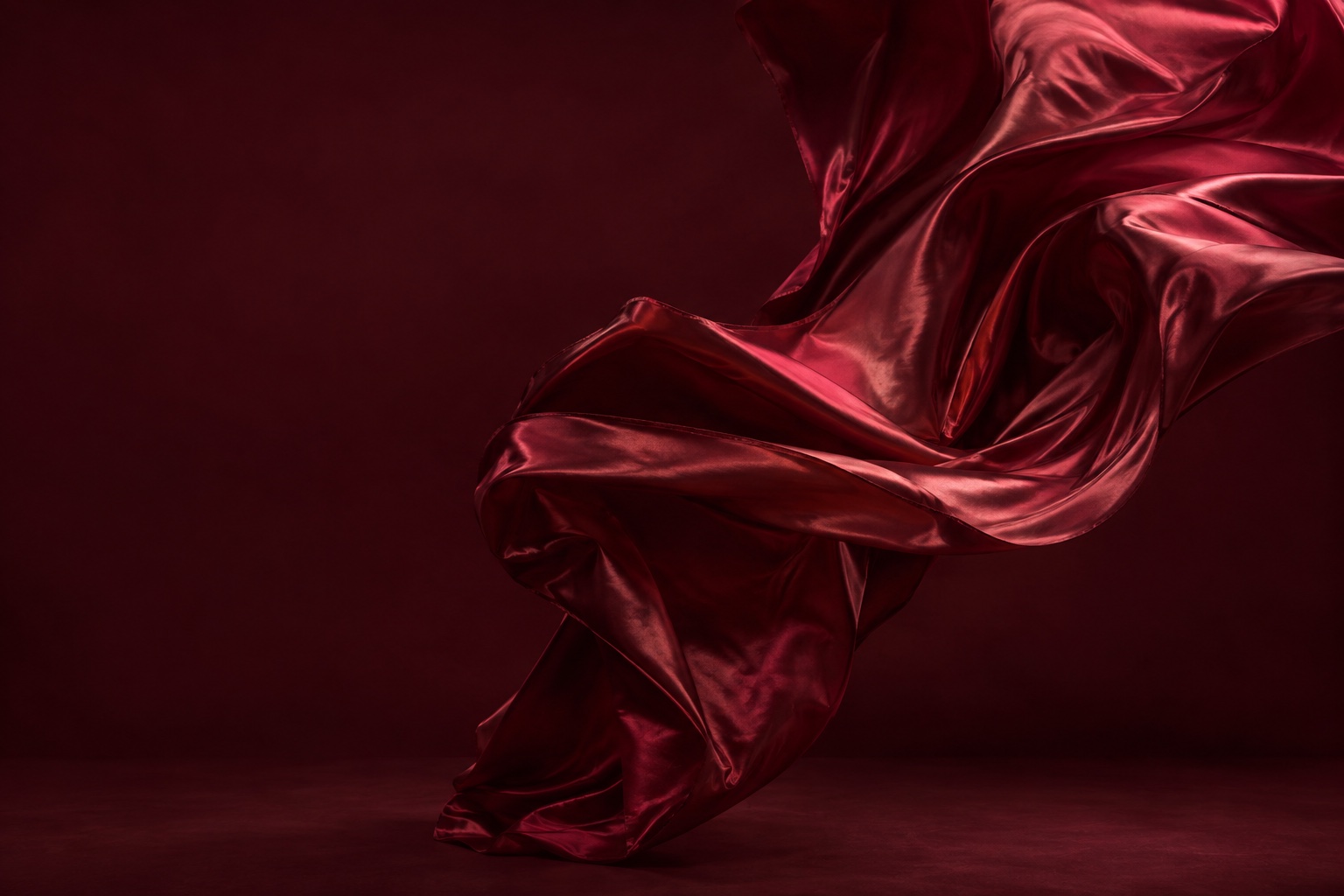 Oxblood silk sweeping through a sculptural curve in a dramatic studio setting